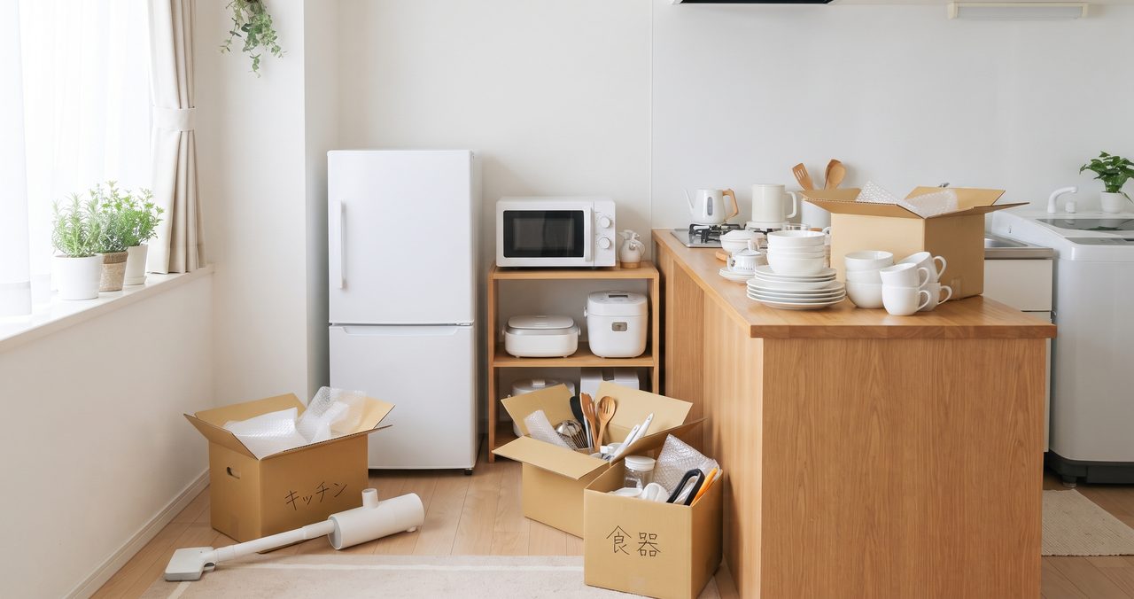 冷蔵庫や電子レンジ、カウンターのある台所で、食器の入った段ボールを整理する様子