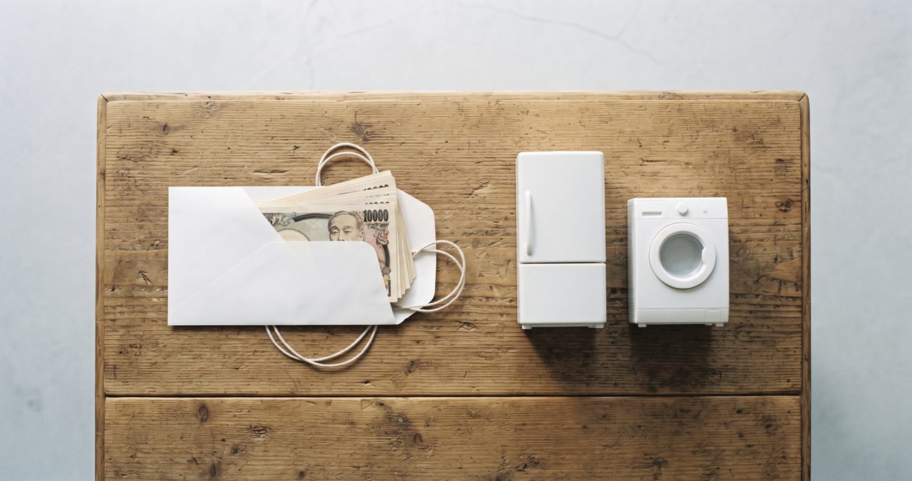 封筒に入ったお金と家電のミニチュアを天秤のように並べ、手当でどこまで初期費用をまかなえるかを示すイメージ