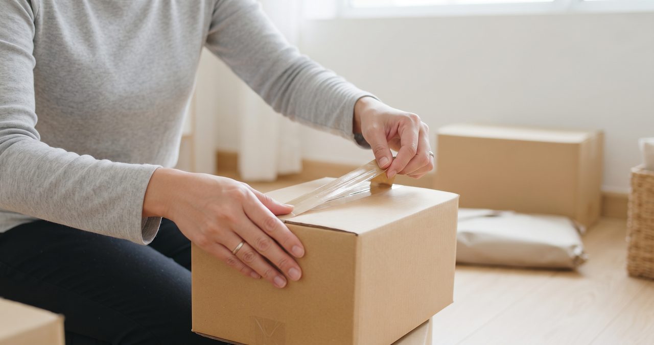 小さな無地の段ボール箱をガムテープで封をしている手元、保留にした荷物を保管用に梱包する様子