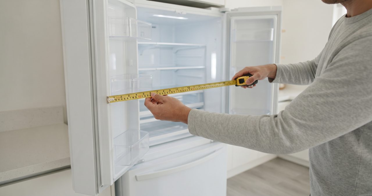 観音開き冷蔵庫の扉を開けた状態で、扉を含めた奥行きをメジャーで測っている手元のクローズアップ